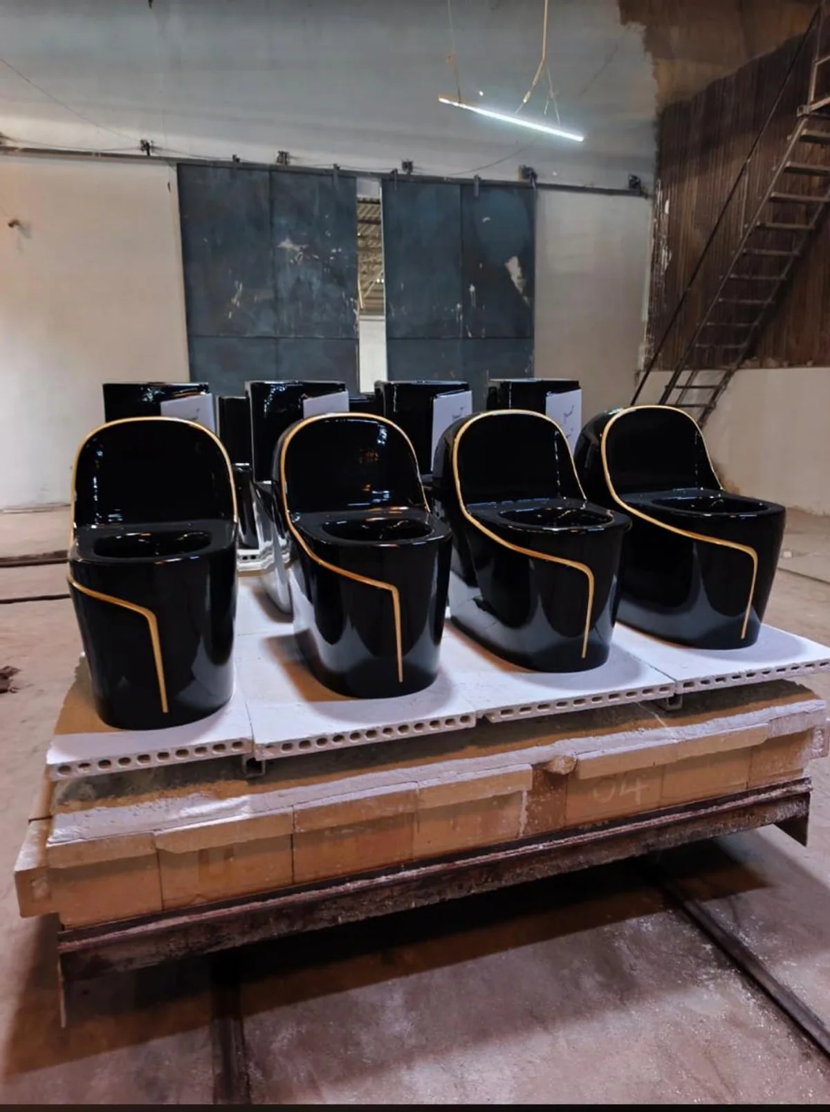 Black one-piece toilets with gold trim on a kiln car